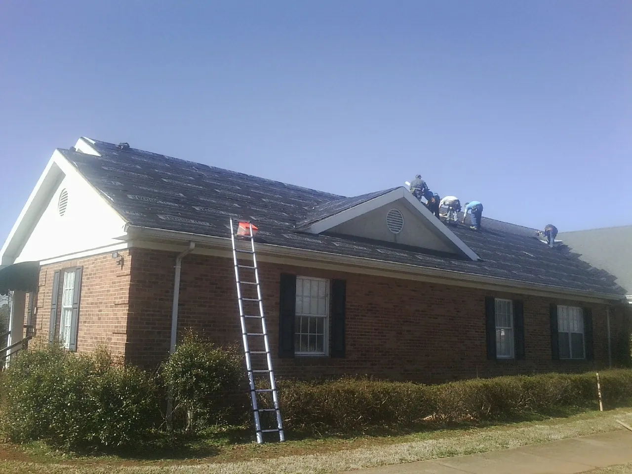 Crew tearing shingles off a brick ranch roof with a ladder set — Emergency Roof Repair work by our crew in Vernonia
