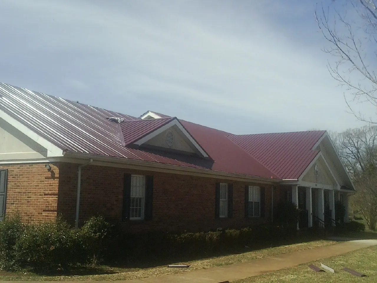 Red metal roof with gabled entries on a long brick building, from a Hail Damage Roof Repair job in Vernonia