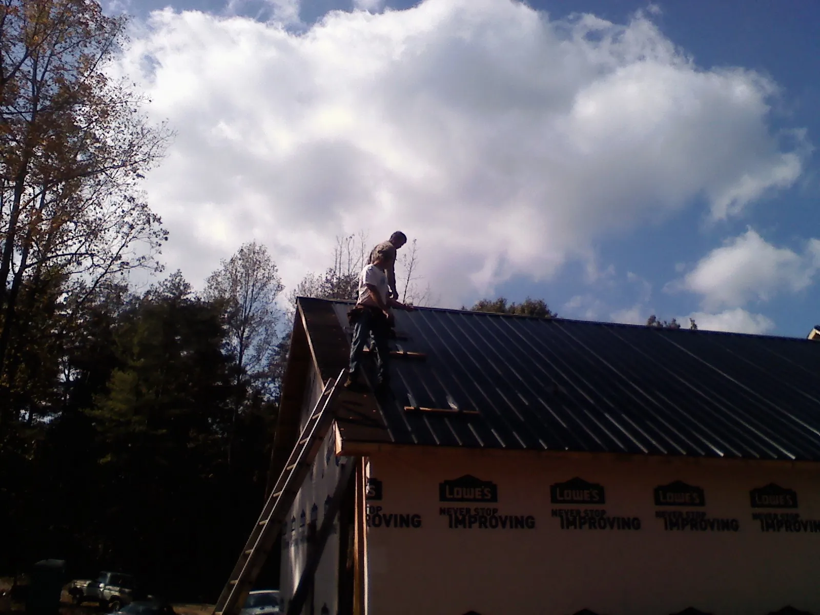 Roofer fastening dark metal panels high against a cloudy sky, from a Roof Inspection job in Vernonia
