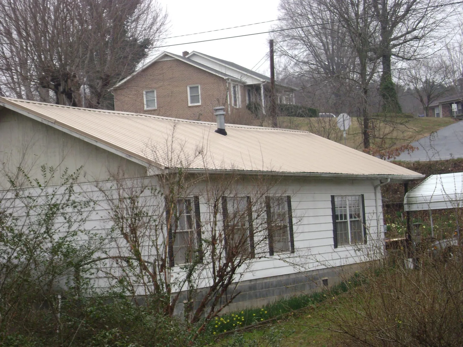Tan metal roof on a white sided house set into a hillside — Commercial Roofing by Roofing Brothers in Vernonia